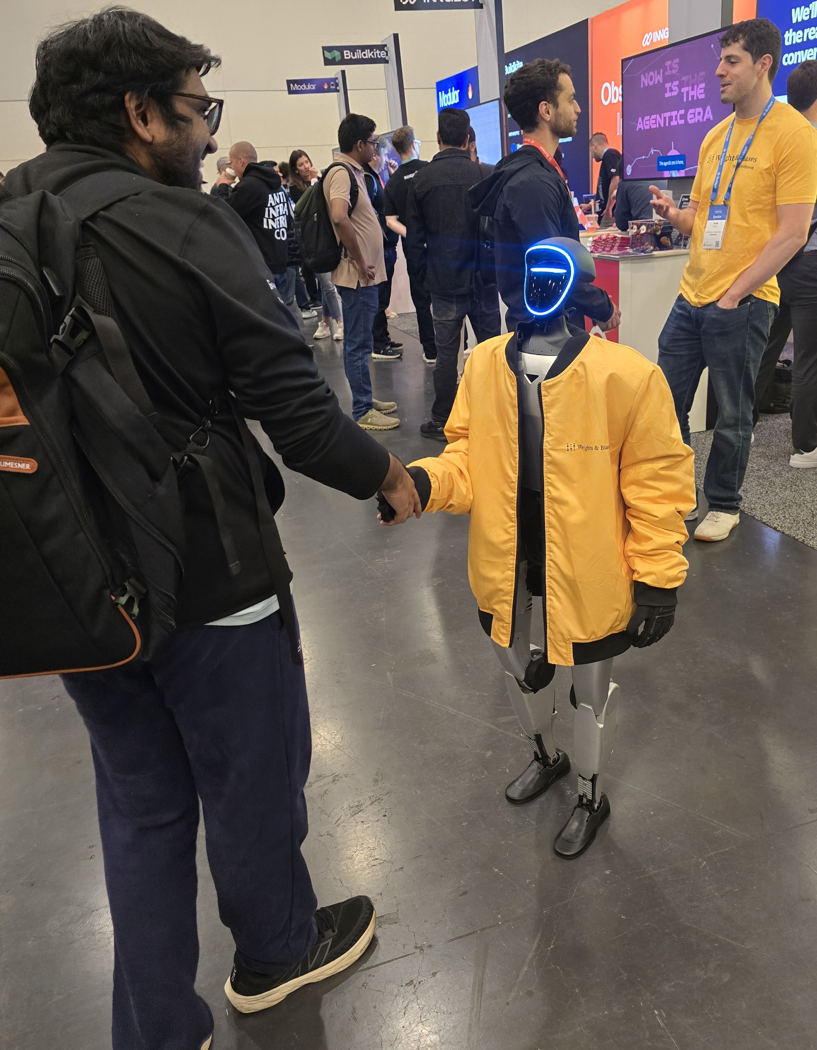 A Weights & Biases branded humanoid robot shaking hands with an attendee on the expo floor