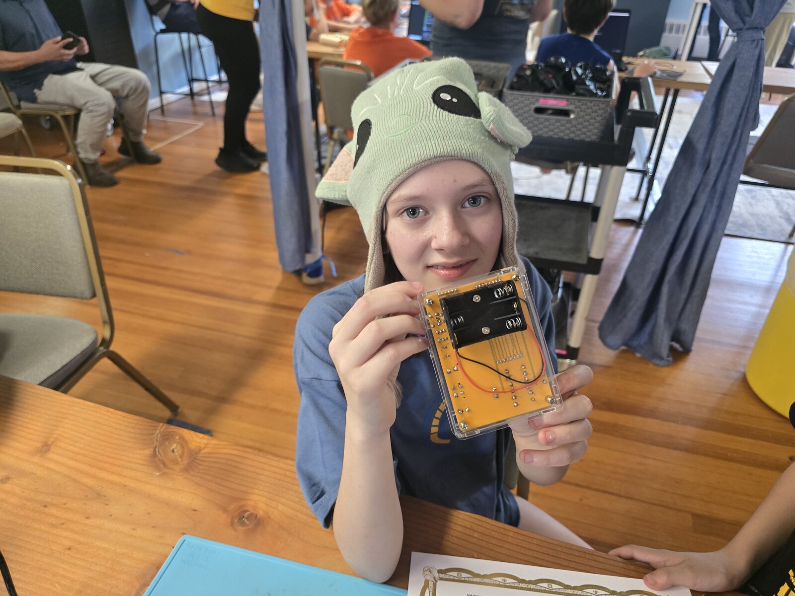 pixie_technologist holding her partially assembled soldered game-boy-like device at camp